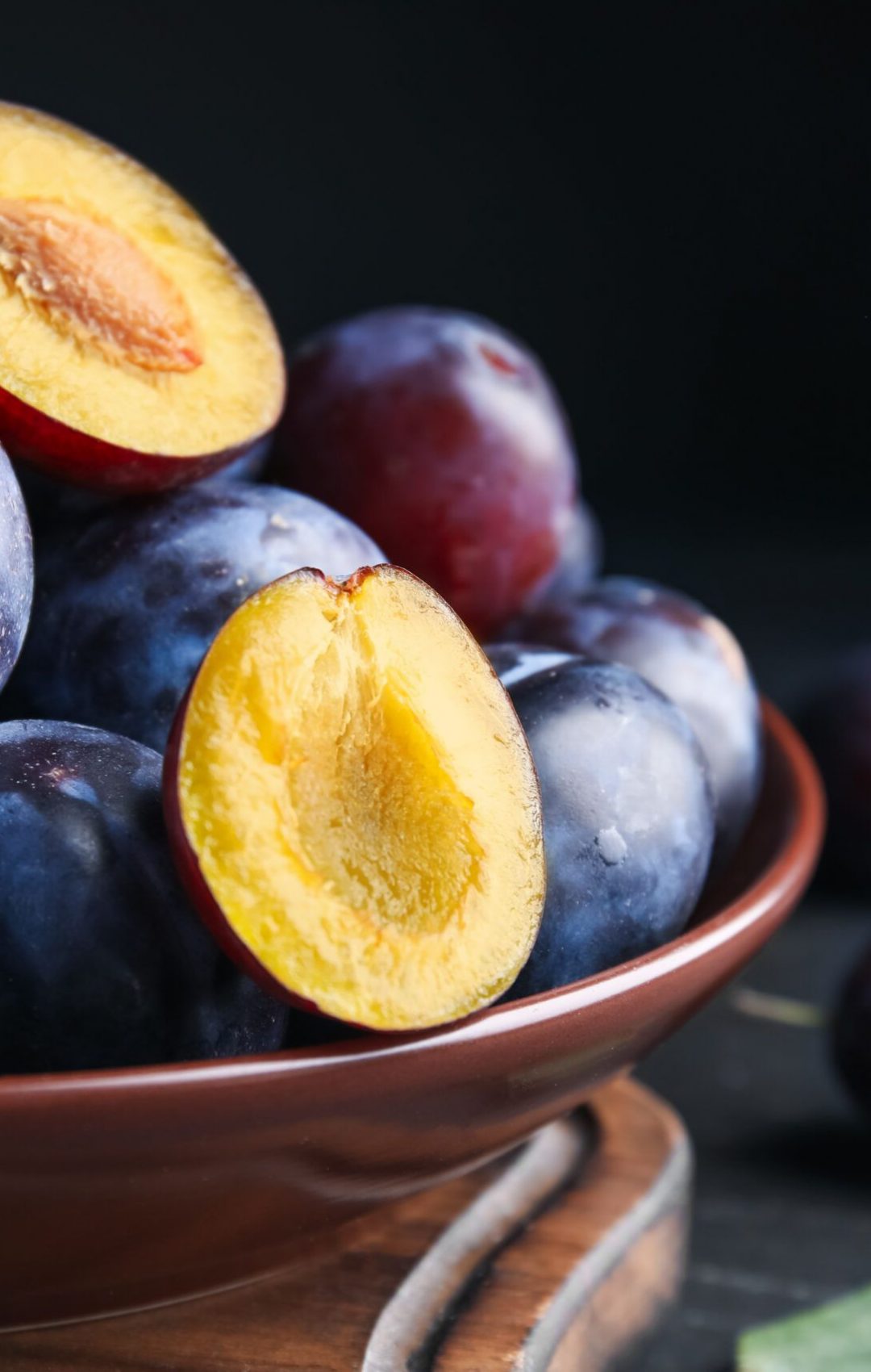 Delicious ripe plums in bowl on black table, closeup